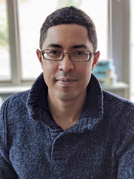 David A T Önaç wearing black glasses and a navy sweater, smiling gentlu at the camera